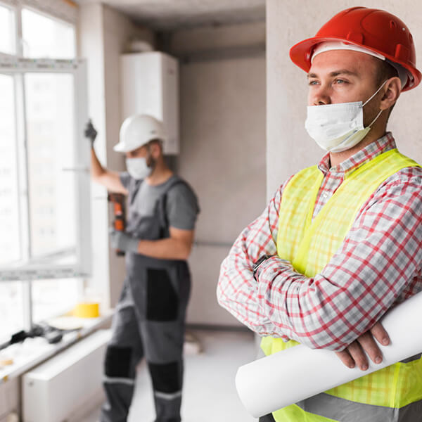 Técnico de obra mirando hacia adelante con un empleado trabajando en una ventana en el fondo