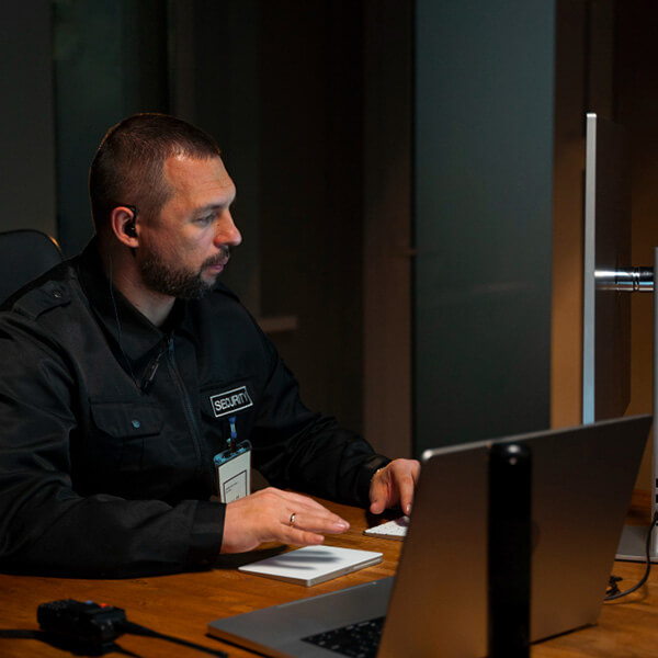 Empleado de empresa de seguridad sentado en un ecritorio trabajando con un ordenador personal adelante